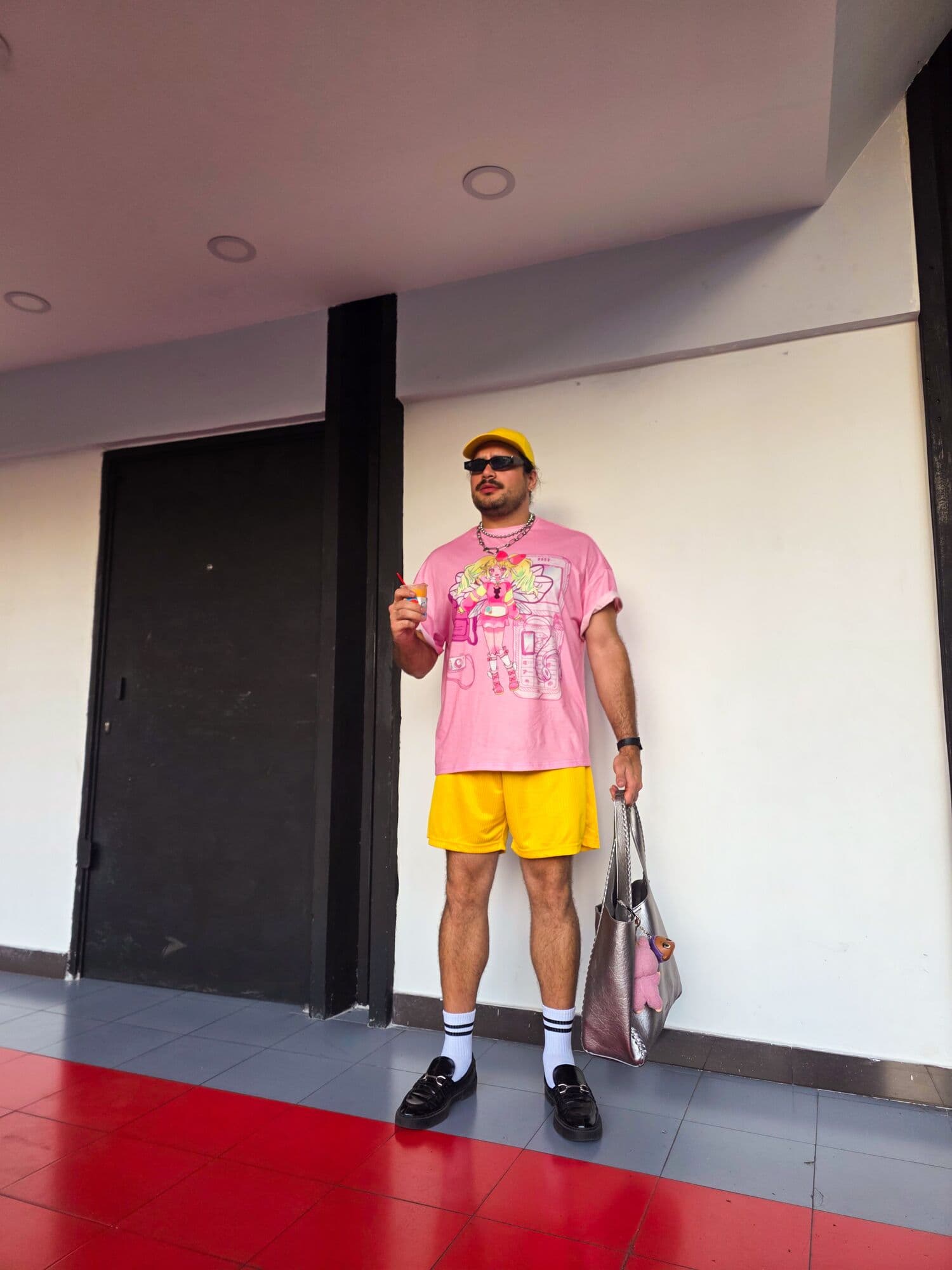 Yisus con camiseta rosa, short amarillo y calcetas blancas frente a una pared blanca
